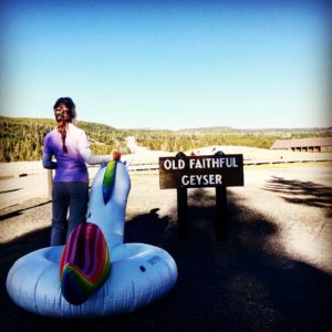 a woman standing next to old faithful with an inflatable unicorn