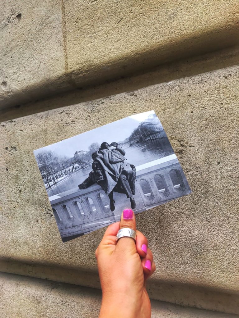 hand holding a postcard of a couple kissing on a bridge